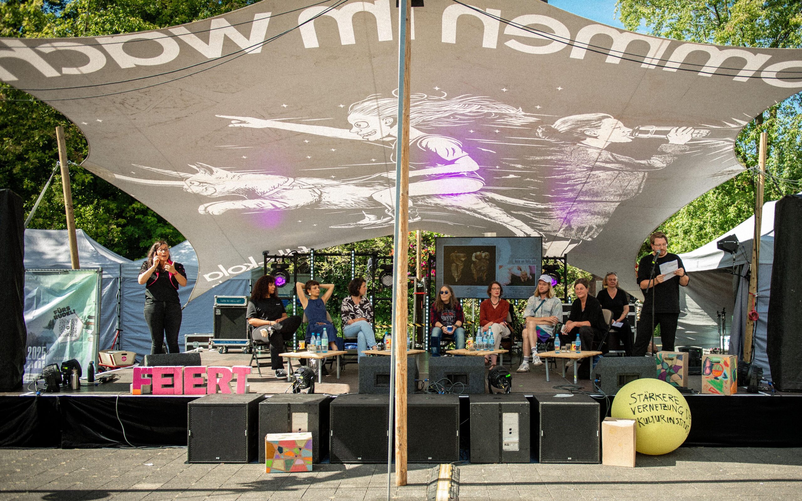 Panel-Veranstaltung. Mehrere Personen sitzen auf einer Bühne.